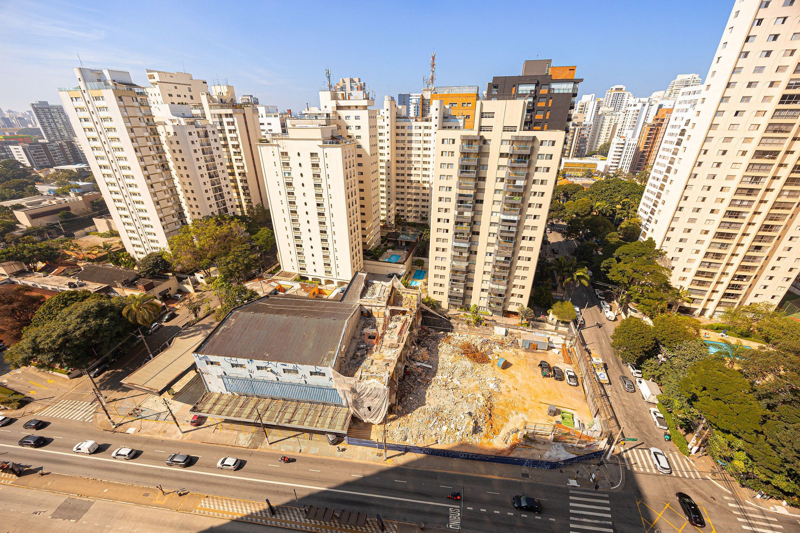A high-rise residential building with multiple balconies, a parking area, and a construction site with debris.