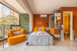 A modern bedroom with a bed, a sofa, a bathroom, and a view of the city. - Hospedez - Estudios Campo Belo Movi (São Paulo)