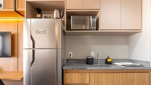 Cocina compacta con refrigerador integrado, microondas y una pequeña encimera con hervidor y cafetera.