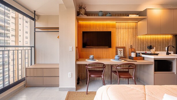 Un dormitorio moderno con una cama grande, un escritorio empotrado y vistas a un paisaje urbano desde un balcón.