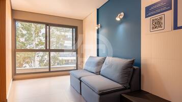 A modern room with a large window, a sofa, a wall-mounted light, and a QR code for instructions.