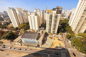 A high-rise residential building with multiple balconies, a parking area, and a construction site with debris. - Hospedez - Estudios Campo Belo Movi (São Paulo)