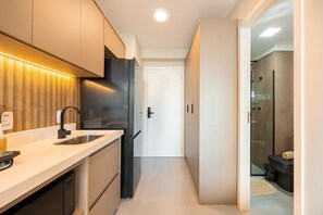 A modern kitchen with a built-in dishwasher, a black refrigerator, and a countertop with a sink. - Hospedez - Estudios Campo Belo Movi (São Paulo)