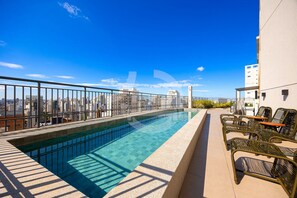 Une piscine sur le toit offrant une vue dégagée sur les gratte-ciel de la ville, avec une rambarde et des sièges d’extérieur.