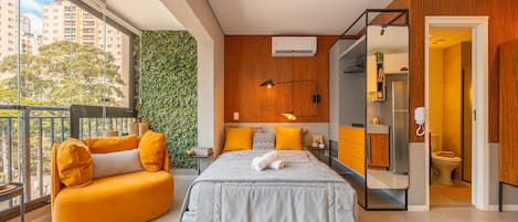 A modern bedroom with a bed, a sofa, a bathroom, and a view of the city.