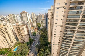 Un immeuble résidentiel de grande hauteur, doté de nombreux balcons, bordé par une rue principale et entouré de verdure.