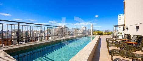 Una piscina en la azotea con vistas despejadas del horizonte urbano, barandilla y mobiliario exterior.