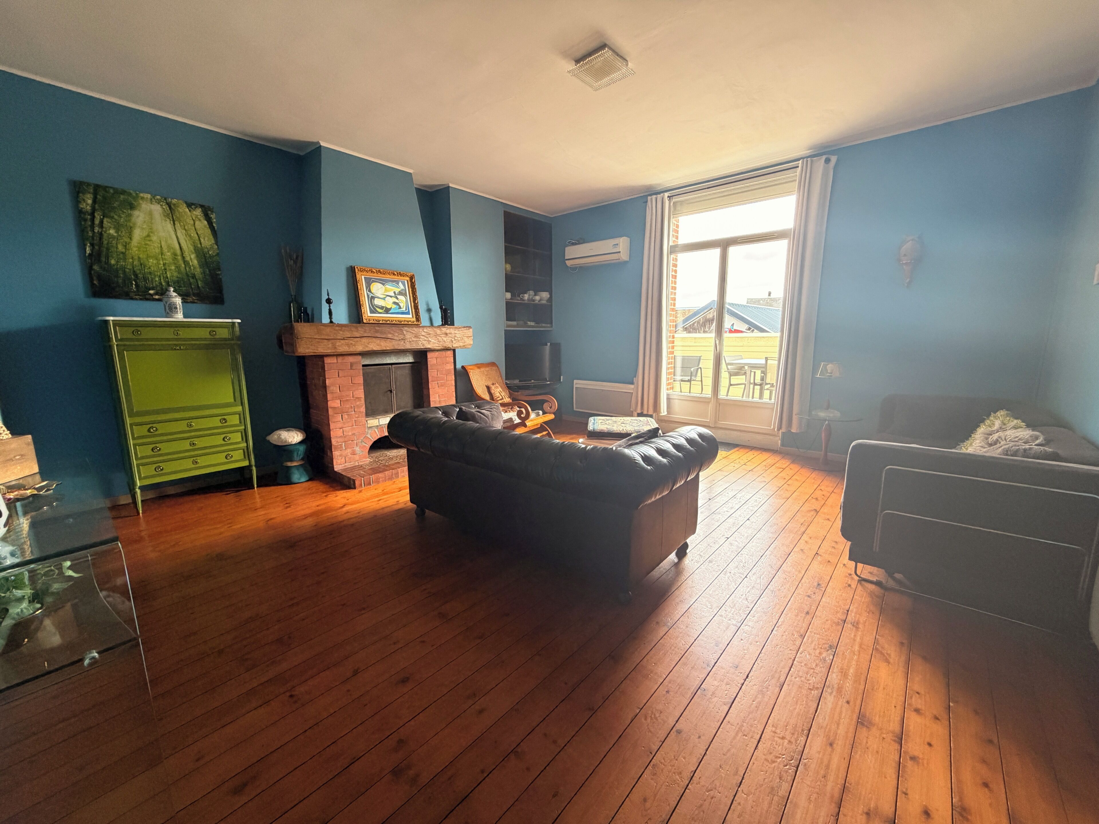 A living room with a fireplace, a sofa, a green dresser, and a view through a glass door.