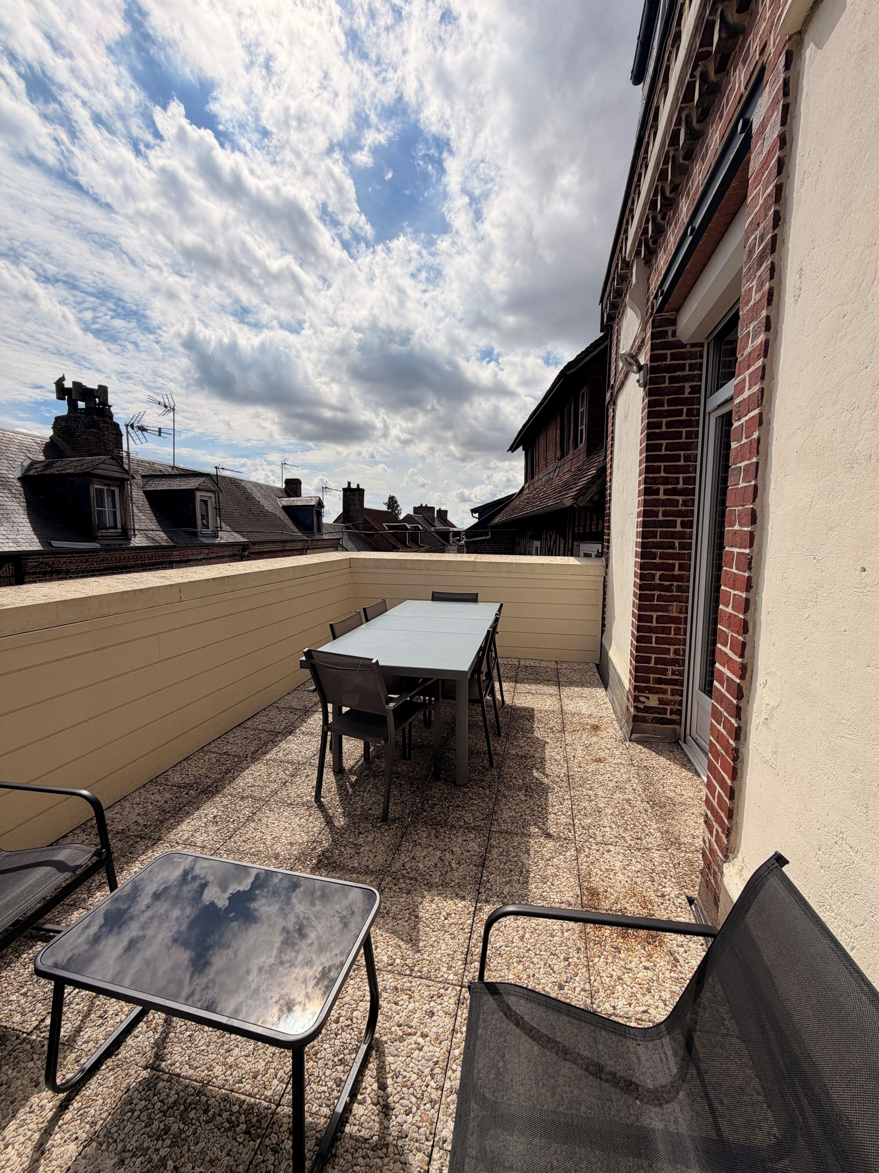 An outdoor patio with a table and chairs, a view of the neighborhood, and a building with a brick facade.
