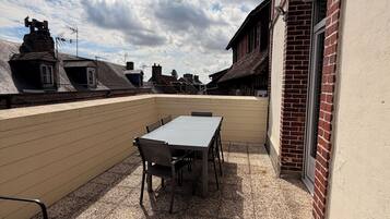 An outdoor patio with a table and chairs, a view of the neighborhood, and a building with a brick facade.