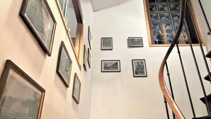 A staircase with a wooden handrail and a glass railing, leading to a landing with framed pictures on the wall.