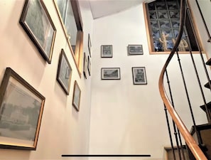 A staircase with a wooden handrail and a glass railing, leading to a landing with framed pictures on the wall.