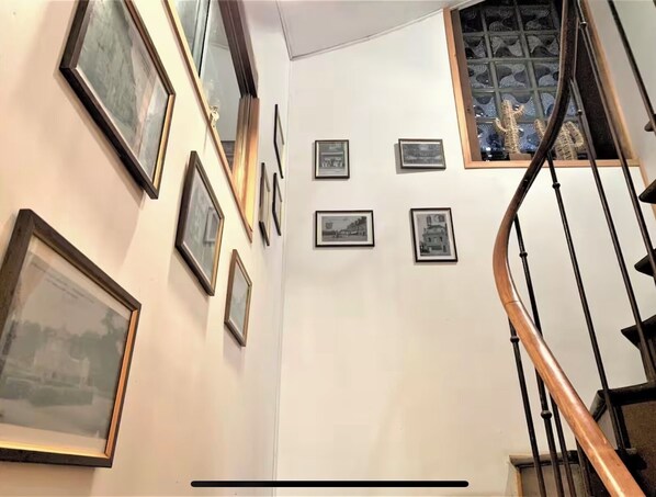 A staircase with a wooden handrail and a glass railing, leading to a landing with framed pictures on the wall.