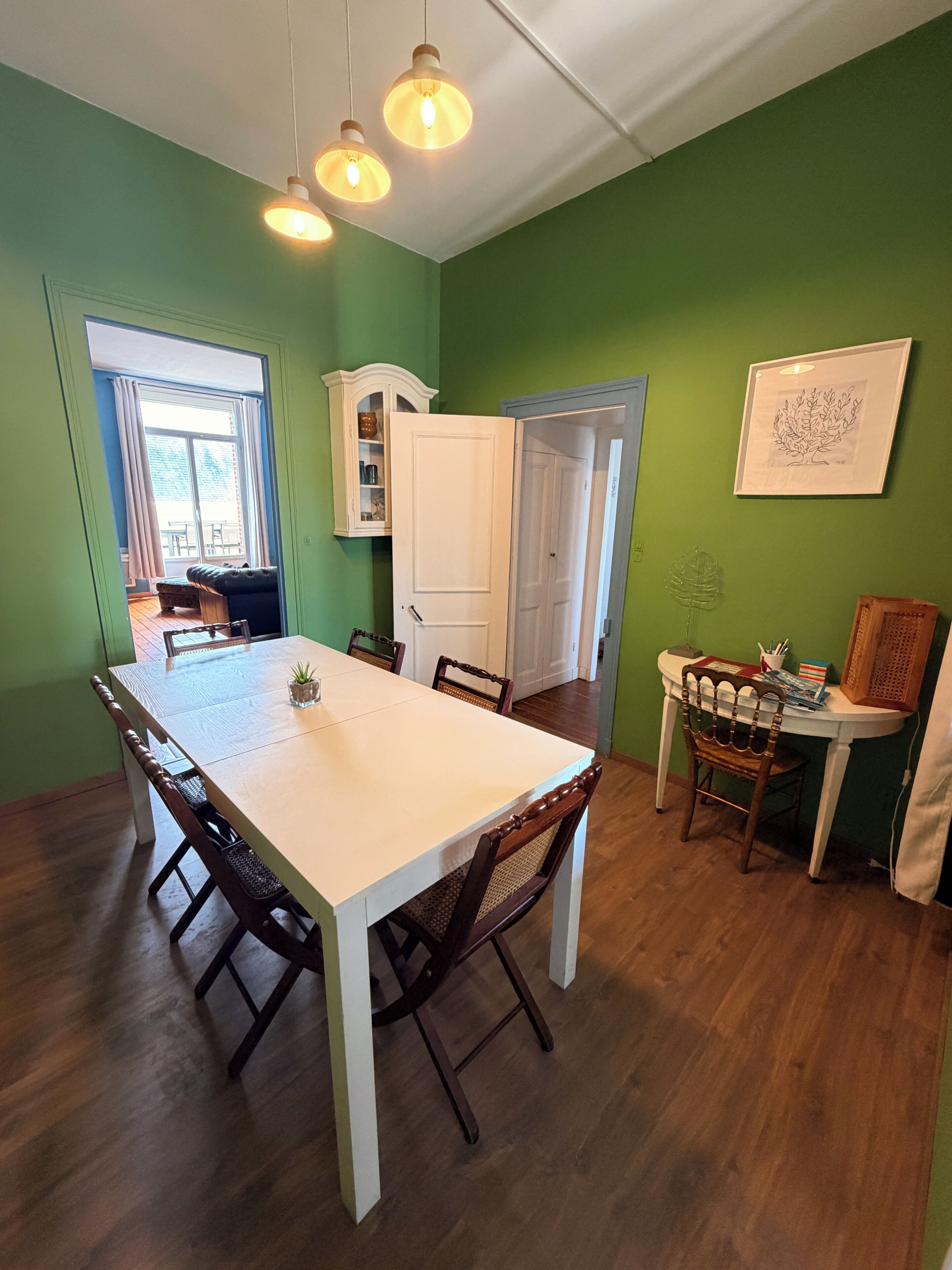 A dining area with a white table, wooden chairs, and pendant lighting.