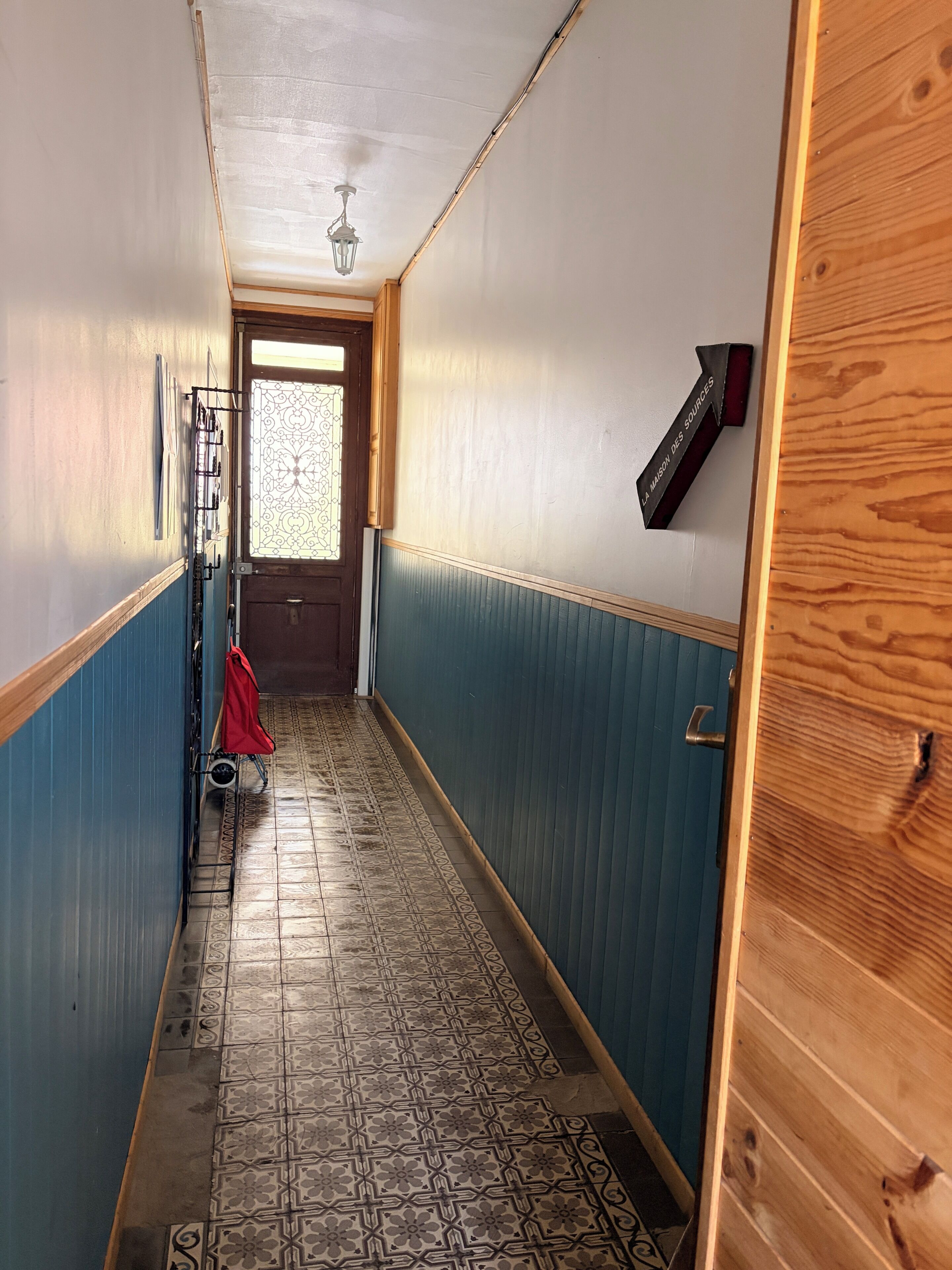 Un pasillo con baldosas de diseño, una puerta de madera y un aplique de pared.