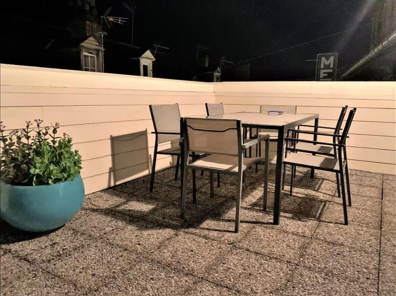 Une terrasse extérieure avec une table et des chaises, une plante en pot et un mur blanc.
