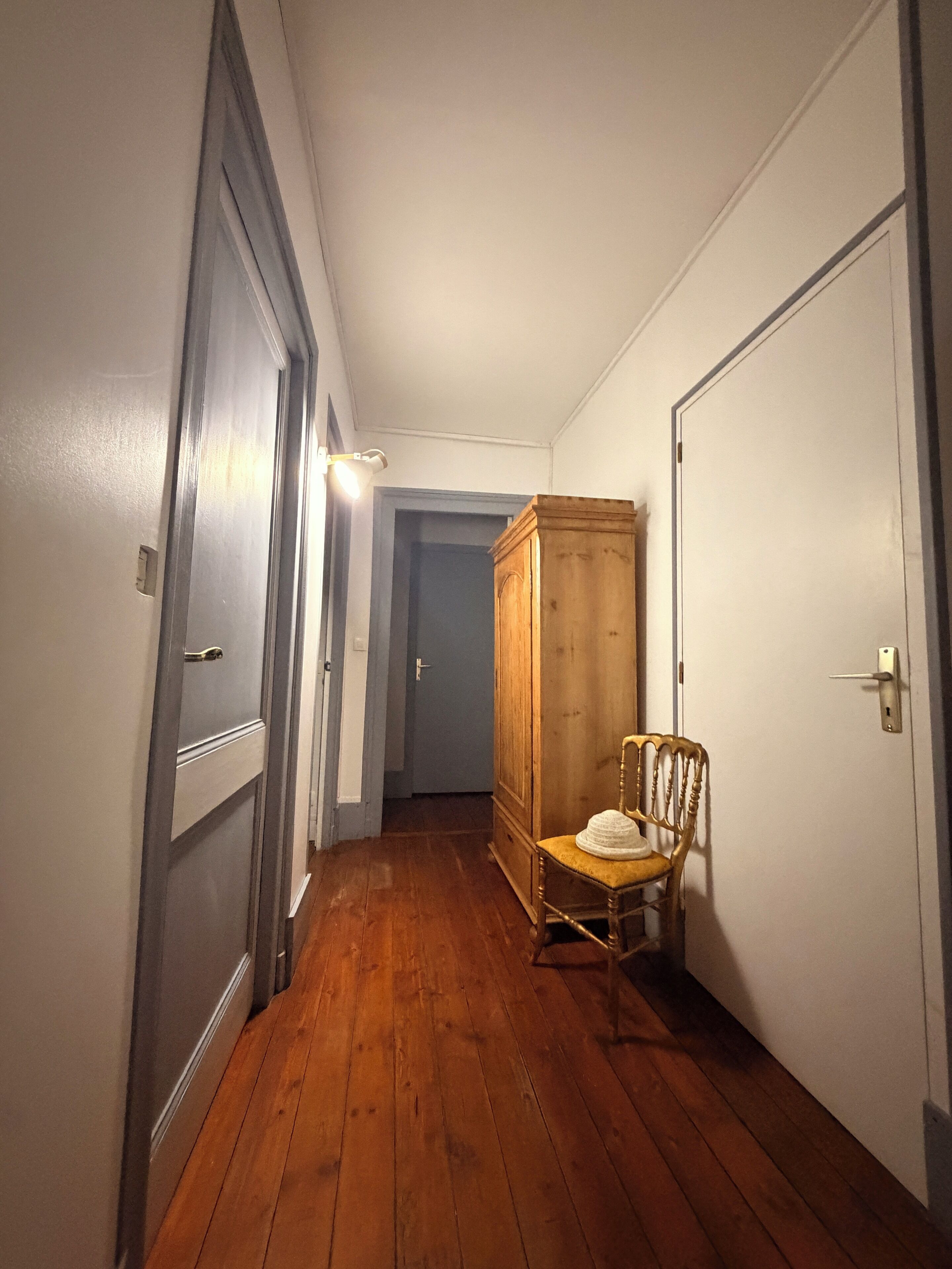 Un couloir avec un plancher en bois, une chaise en bois et une armoire.