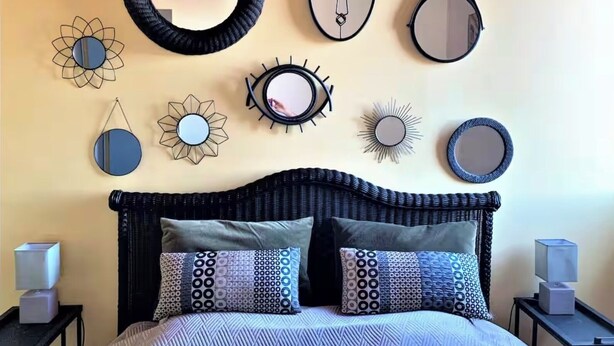 A bedroom with a bed, two nightstands, and various wall decorations including mirrors and sunburst patterns.