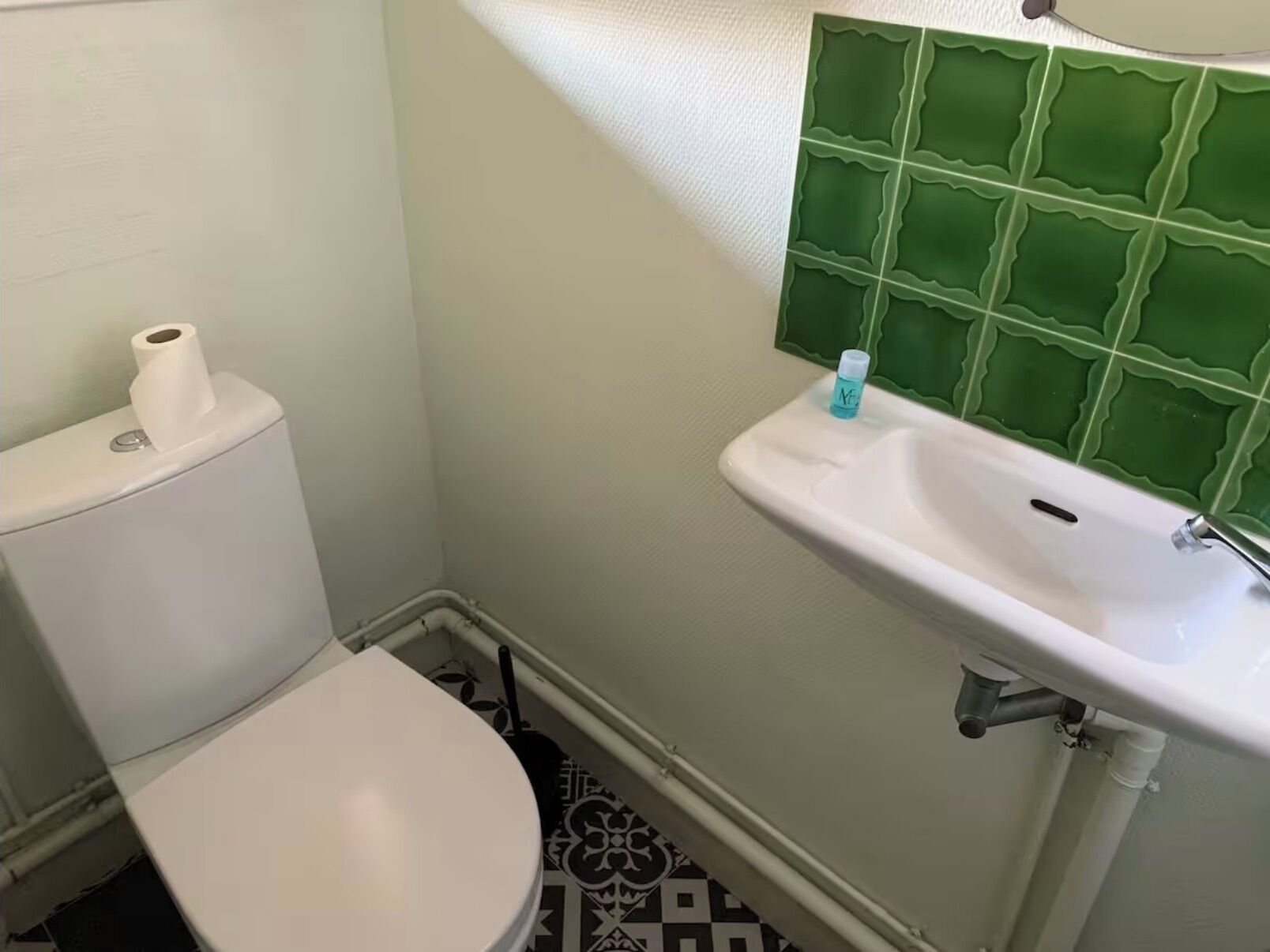 A bathroom with a toilet, sink, and green tiled backsplash.