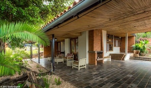 An outdoor covered patio with wicker furniture, a brick fireplace, and a view of the surrounding greenery. - Heaven Restaurant and Boutique Hotel (Kigali)