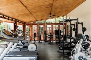 Uma academia com esteiras, aparelhos de musculação e um ventilador de teto.