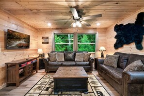 Ein Blockhaus-Innenraum mit Ledersofa, Couchtisch, Fernseher und aufgehängtem Tierfell.