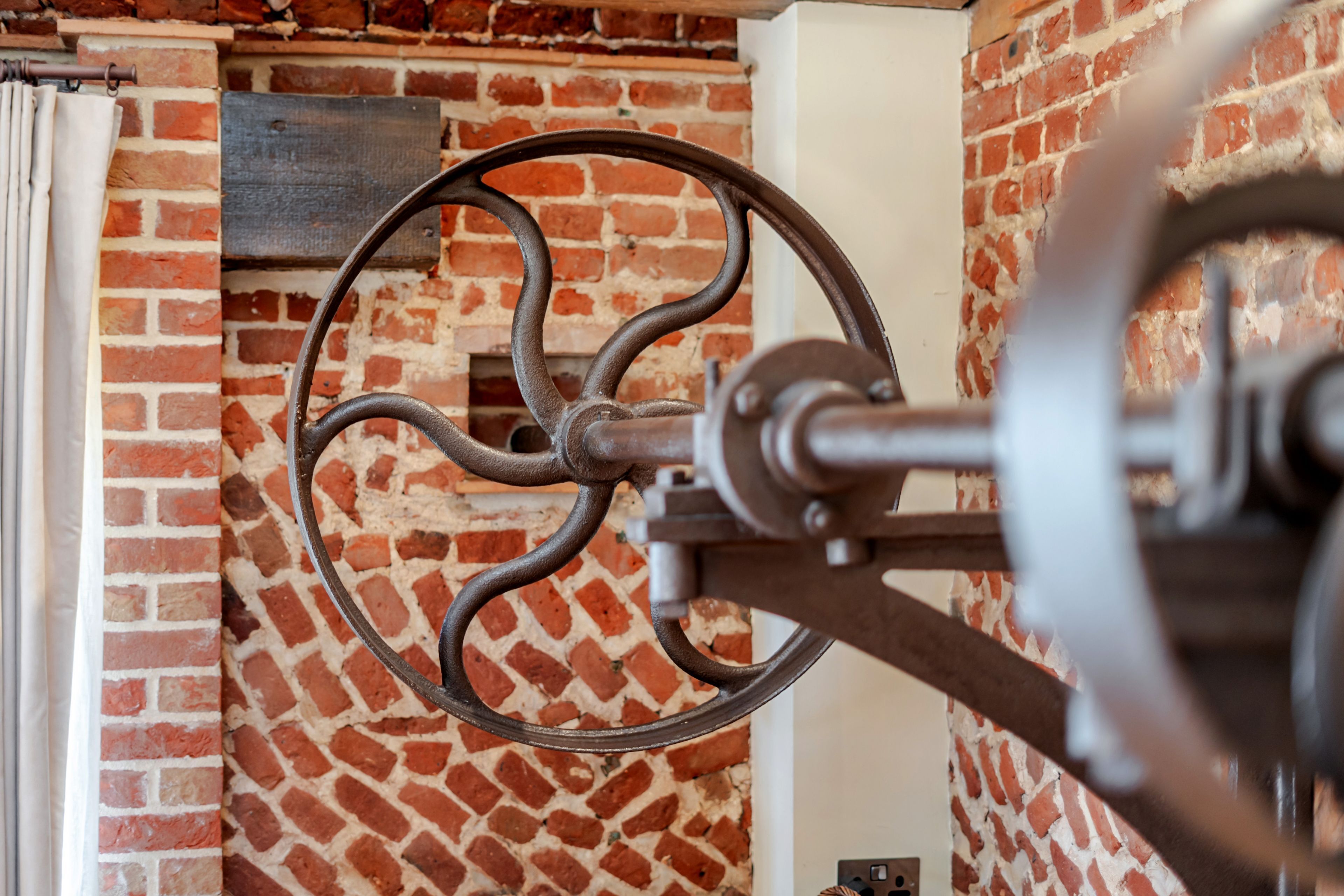 A close-up of a mechanical wheel, possibly part of a machine, against a brick wall.