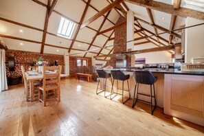 A spacious kitchen with wooden beams, a brick wall, and a large island with bar stools. - High Barn - sleeps 8 guests  in 4 bedrooms (Binham)