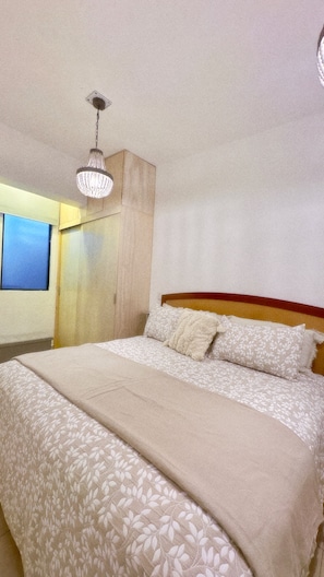 Un dormitorio con cama, lámpara de araña, armario y ventana.