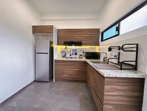 Una cocina compacta con gabinetes de madera, un refrigerador de acero inoxidable, un microondas y un lavamanos.