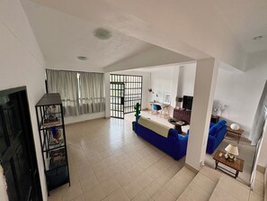 A spacious living room with a blue sofa, a television, and a bookshelf.