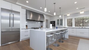 A modern kitchen with stainless steel appliances, a central island with bar stools, and large windows.