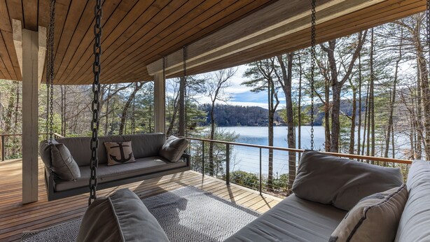 A wooden deck with a swing and a sofa overlooking a lake.