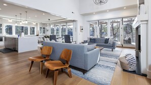 A spacious living area with a grey sofa, wooden chairs, a dining table, and a kitchen in the background.