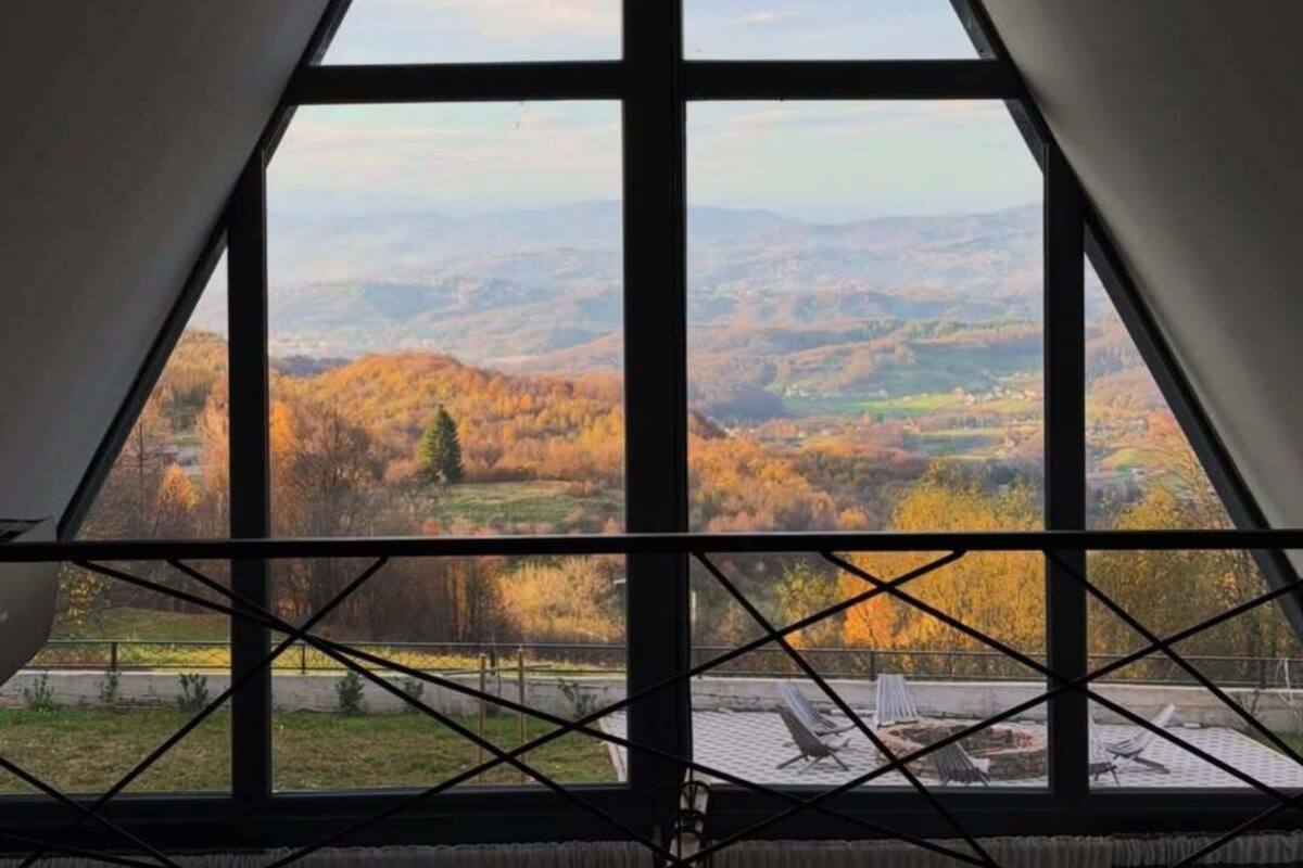 Una habitación con un amplio ventanal triangular que ofrece vistas a un valle con follaje otoñal.