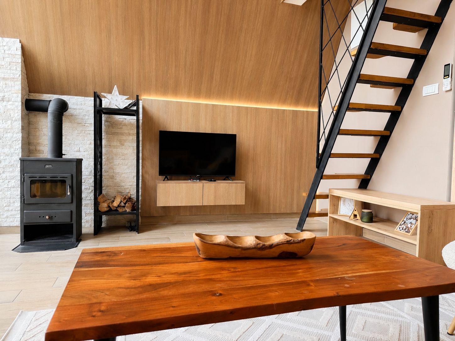 Uma sala de estar moderna com piso de madeira, uma TV fixada na parede, lareira e uma mesa de jantar de madeira.