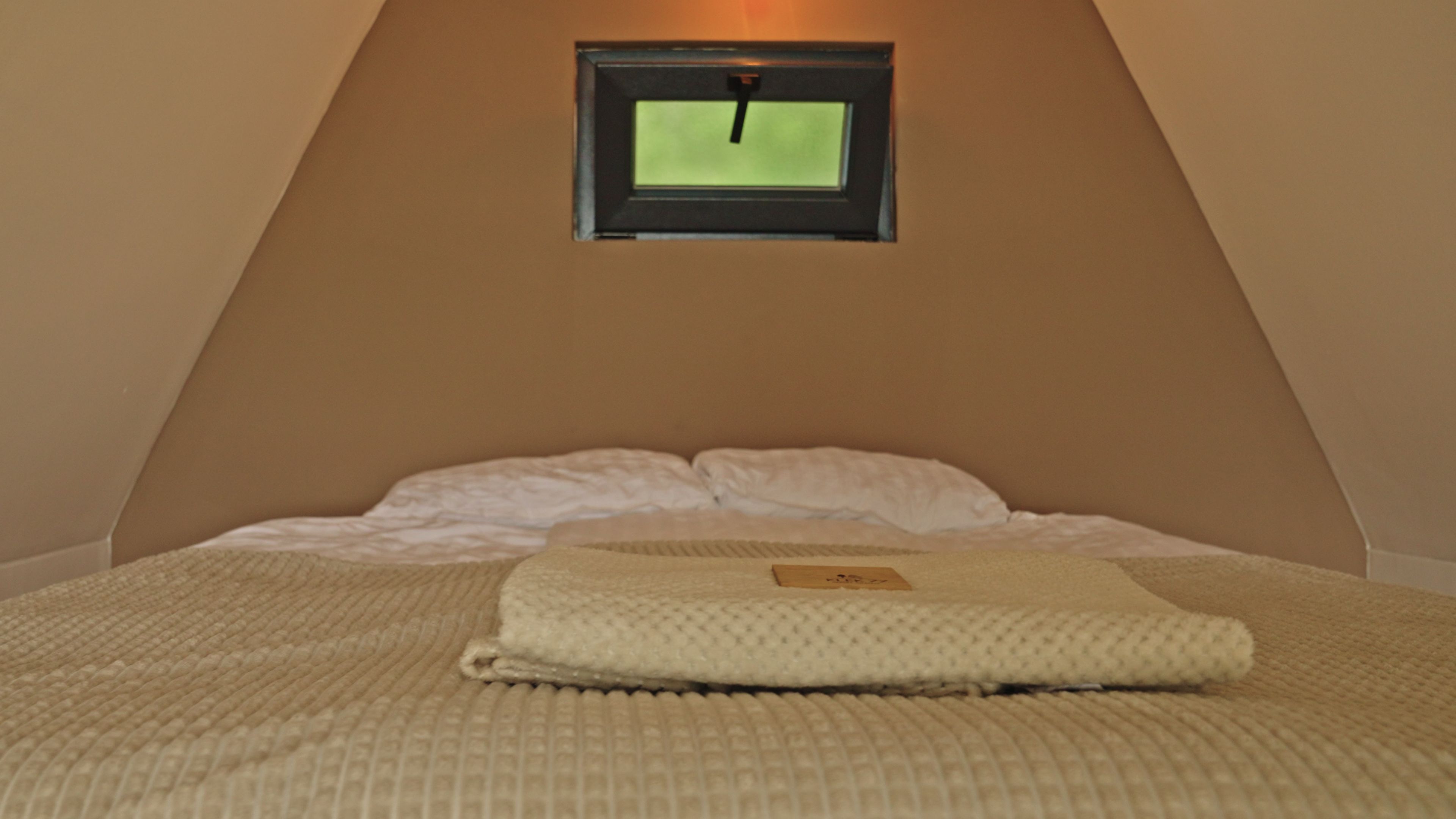 A bedroom with a bed, pillows, a blanket, and a window with a clock.