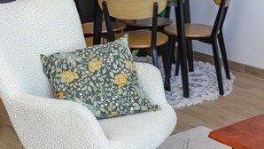 Uma área de refeições acolhedora com uma mesa redonda, cadeiras, uma almofada floral em uma cadeira e um vaso com planta.