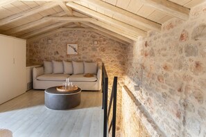 Ein gemütliches Dachzimmer mit Steinwand, einer Couch und einem runden Couchtisch.