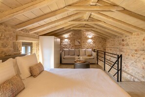 Ein gemütliches Schlafzimmer im Dachgeschoss mit Steinwand, einem Bett mit gemusterten Kissen, einer Couch und einem kleinen runden Tisch.