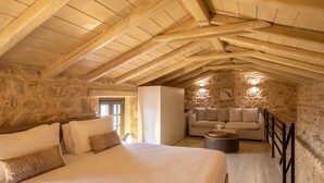 A cozy attic bedroom with a large bed, a sofa, and a stone wall.