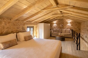 A cozy attic bedroom with a large bed, a sofa, and a stone wall. - Korona Boutique Hotel - Executive Suite (Oitylo)