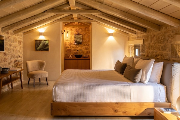 Une chambre confortable avec un lit en bois, un mur en pierre, un petit lavabo et une chaise.