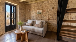 A stone-walled room with a sofa, a small wooden table, and a staircase.