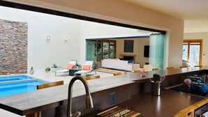 Et moderne køkken med en stor ø, swimmingpool integreret i huset, og et spiseområde med pejs.