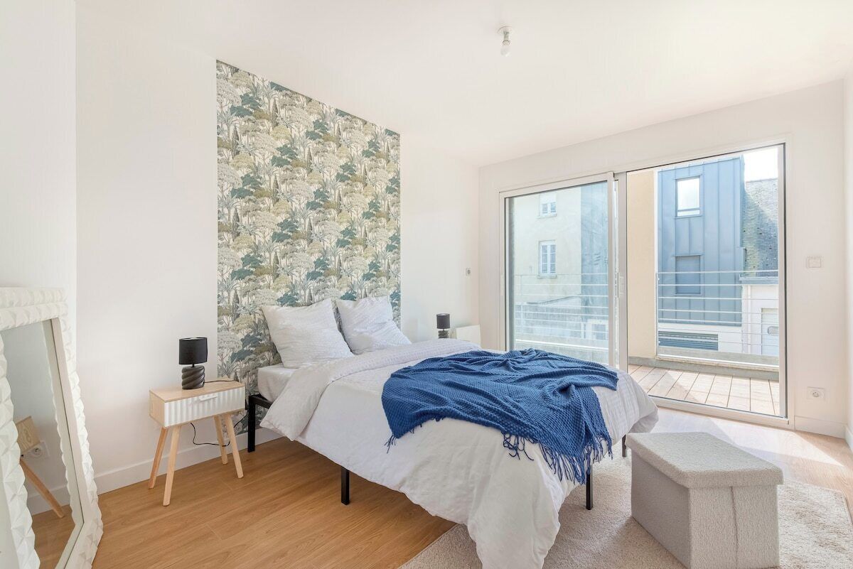Une chambre à coucher avec un lit, des tables de chevet, un miroir, une fenêtre et une vue sur l’extérieur.