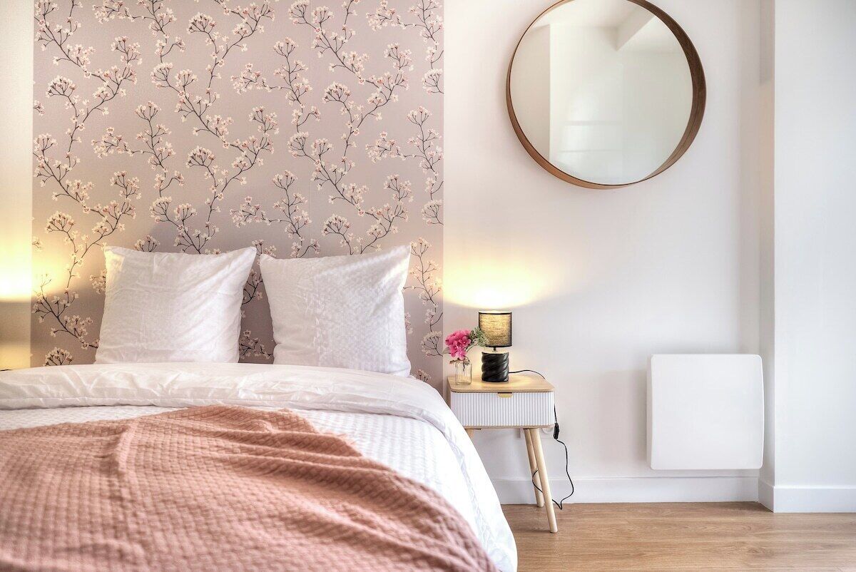 Ein Schlafzimmer mit einem Bett, einem Nachttisch mit Lampe, einem runden Spiegel und einer Heizung.