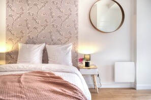 Ein Schlafzimmer mit einem Bett, einem Nachttisch mit Lampe, einem runden Spiegel und einer Heizung.