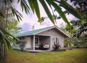 A single-story house with a covered porch, a small garden, and a view of the surrounding greenery. - Koa + Paka: Embrace the elements in style (Keaau)