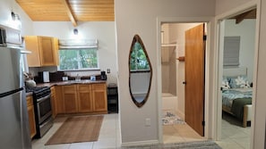 A compact kitchen with wooden cabinets, a stove, and a window with a view of trees. - Koa + Paka: Embrace the elements in style (Keaau)